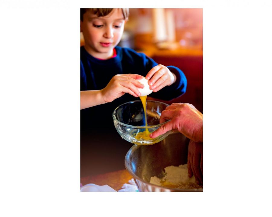 A young boy is learning how to make eggs with the help of his teacher.